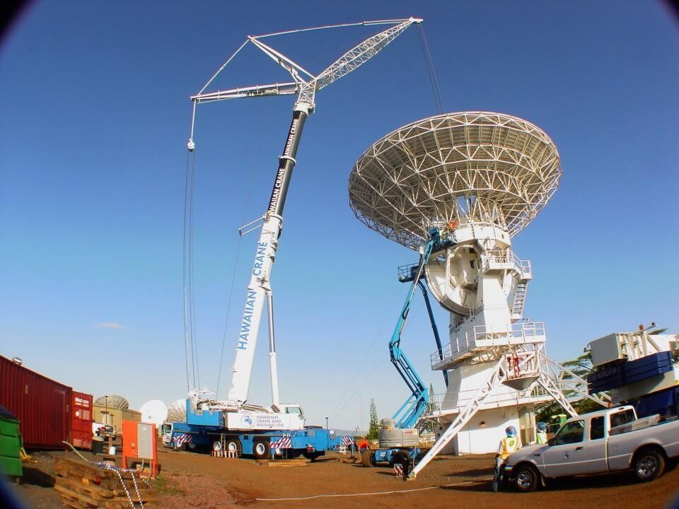 A crane positioning equipment beside a large satellite dish