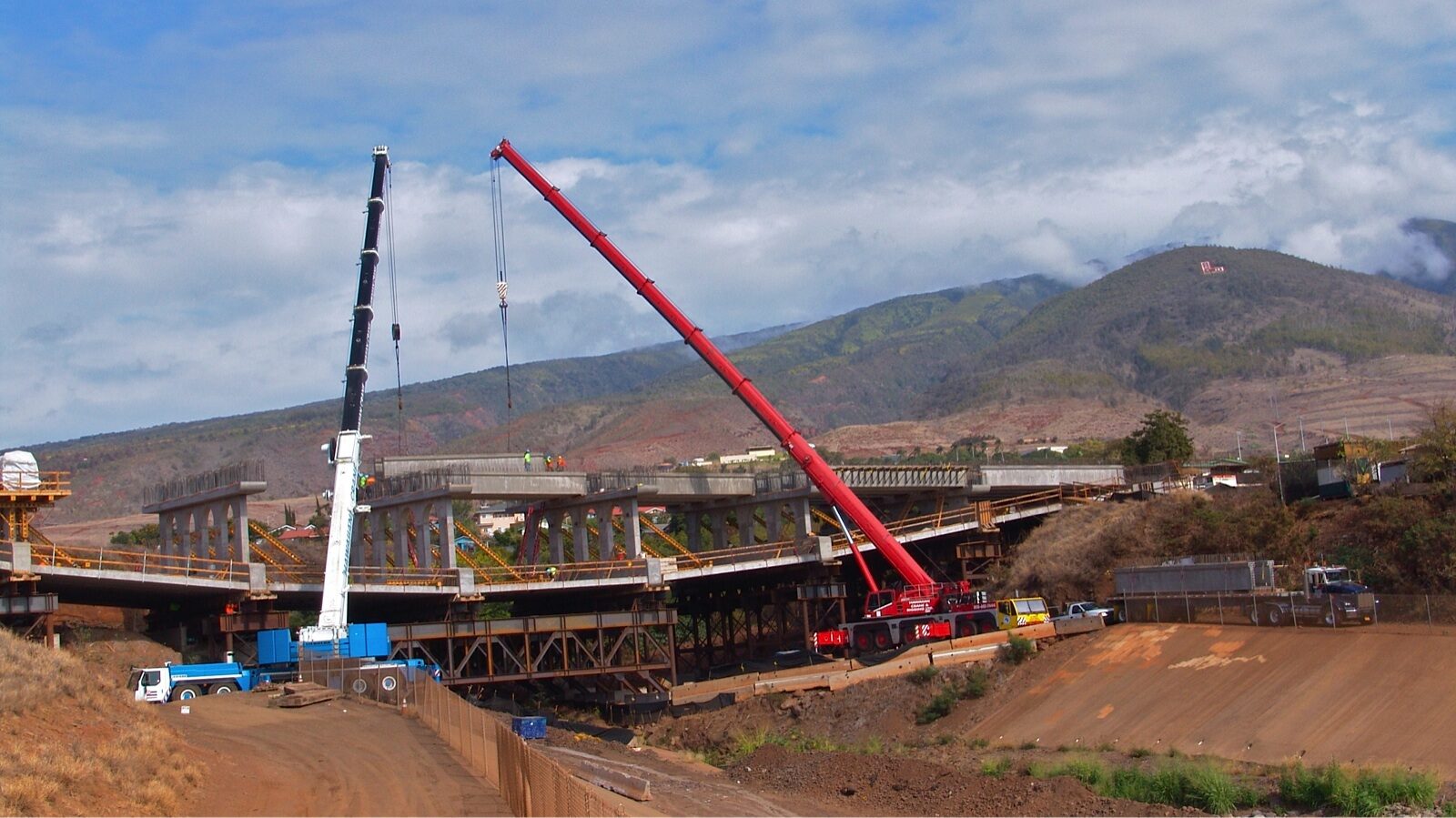 Two cranes operating on a construction site near the mountains